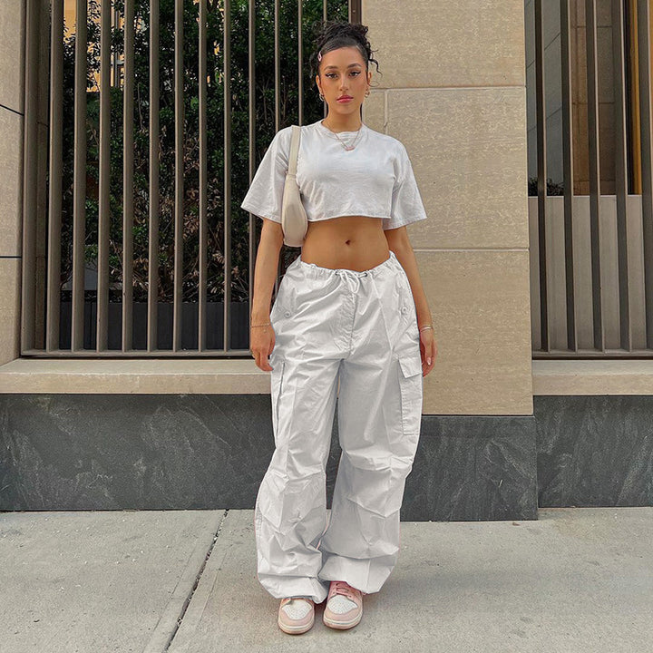 Casual outfit featuring a cropped gray t-shirt and white cargo pants, styled with pink sneakers, showcased outside against a modern architectural backdrop.