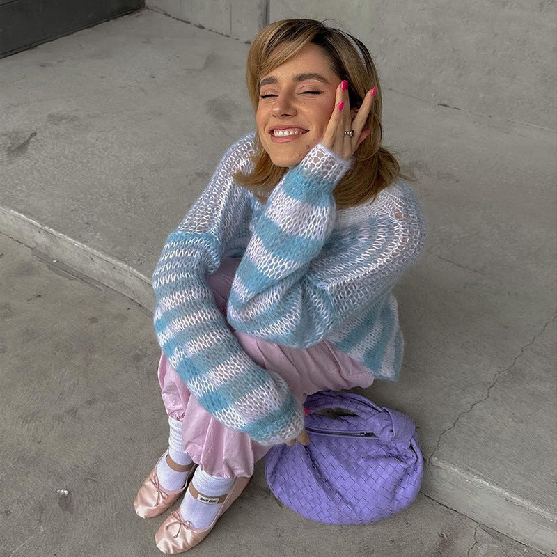 Model in a cozy blue and white striped sweater, pink pajama pants, and ballet flats, sitting on the ground with a playful smile, holding a lavender handbag.