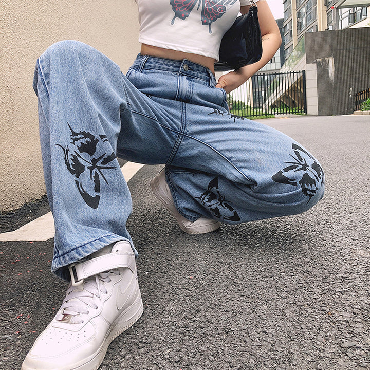 Casual outfit featuring a butterfly print cropped top, high-waisted jeans with butterfly graphics, and white sneakers, captured in an urban setting.