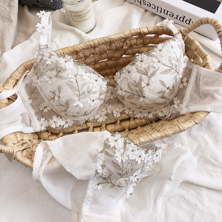 Elegant white lace bra adorned with delicate floral embroidery, paired with a matching sheer lingerie set, all beautifully arranged in a woven basket on a soft fabric backdrop