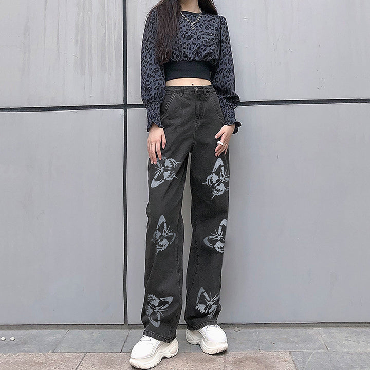 Model wearing a stylish black crop top with leopard print and high-waisted black jeans featuring a butterfly design, paired with white sneakers, set against a modern background.