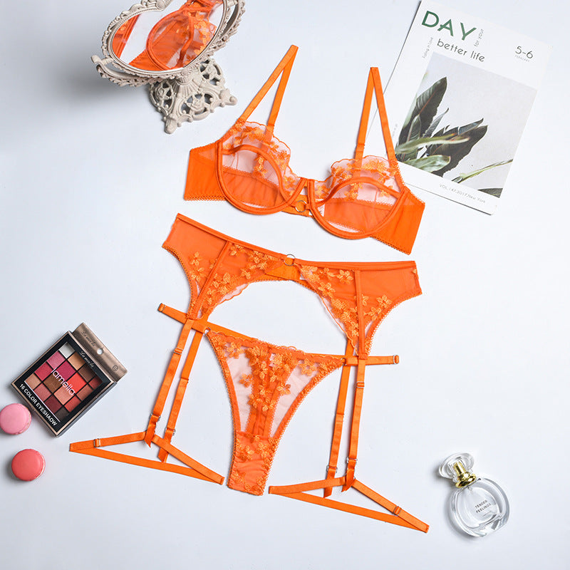 Orange lace lingerie set featuring a bra, garter belt, and thong with floral detailing, styled with cosmetics and perfume.