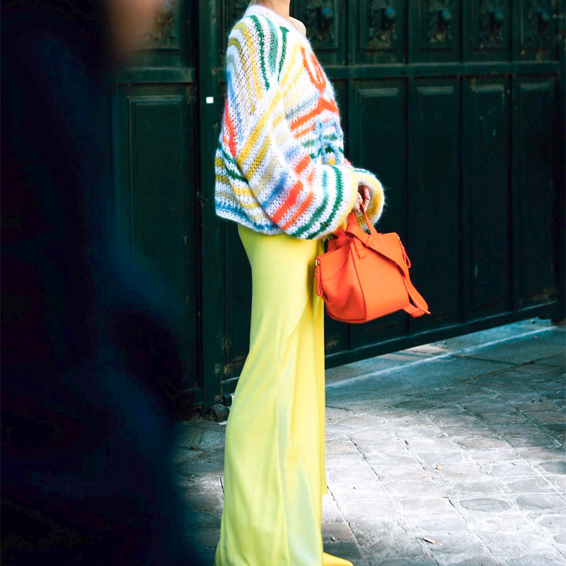 Colorful oversized knit sweater paired with a bright yellow skirt and orange handbag, styled for a chic street look.