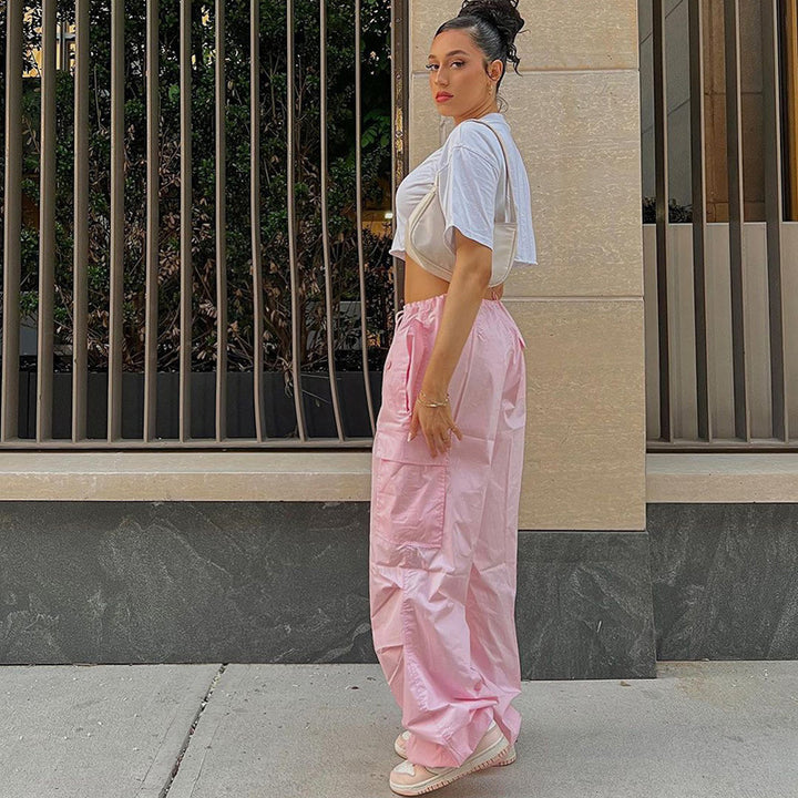 Model wearing a cropped white top and pink satin lounge pants, posing outdoors with a stylish backdrop.