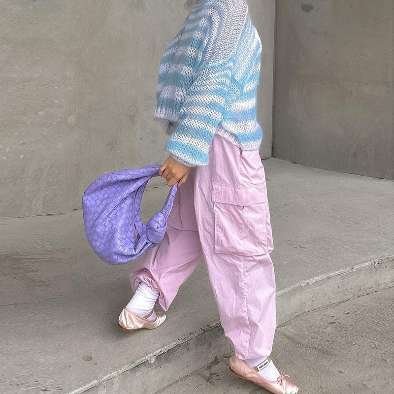 Lingerie model wearing stylish cotton knit top and lightweight cargo pants, accessorized with a purple bag and ballet flats, set against a minimalist background.