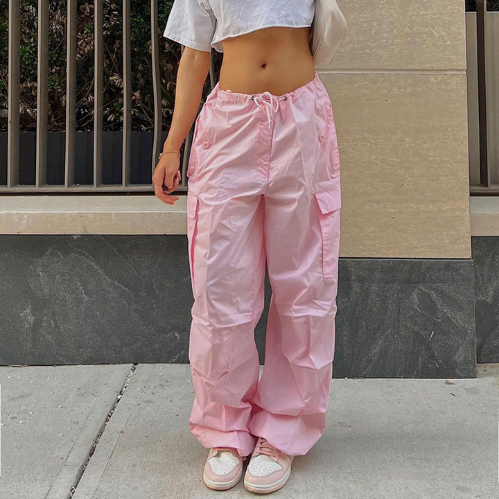 Model wearing a casual white crop top and loose pink cargo pants, paired with white sneakers, standing on a city sidewalk.