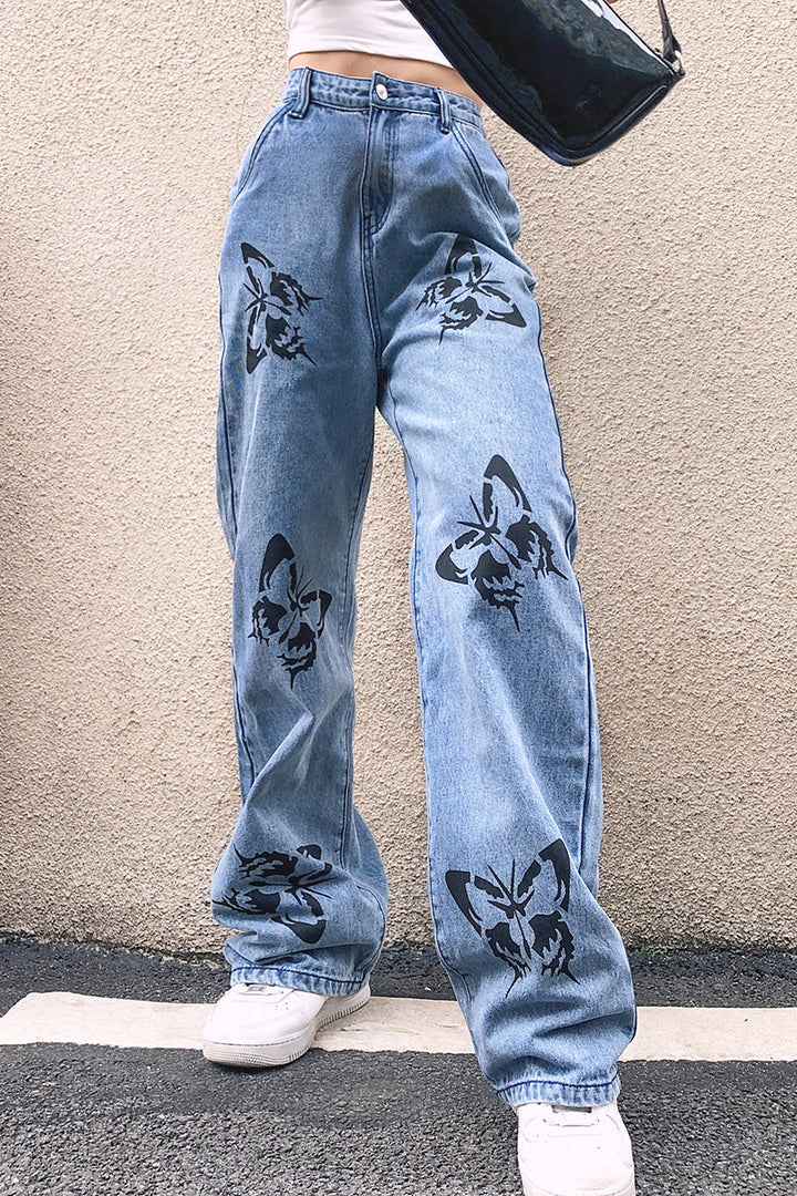 Denim pants featuring black butterfly prints, styled with a cropped top and sneakers, against a neutral wall background.