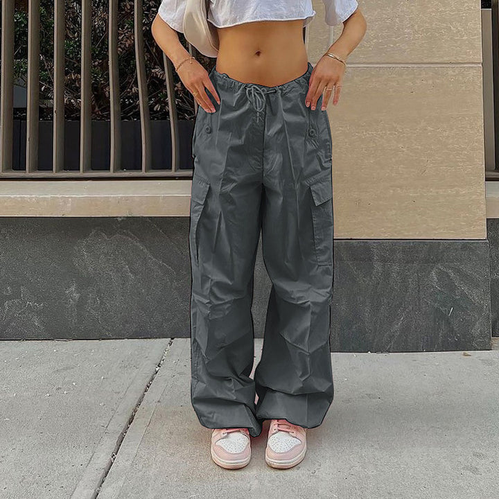 Casual women's olive green cargo pants with adjustable waistband, paired with light pink sneakers, standing on a sidewalk.