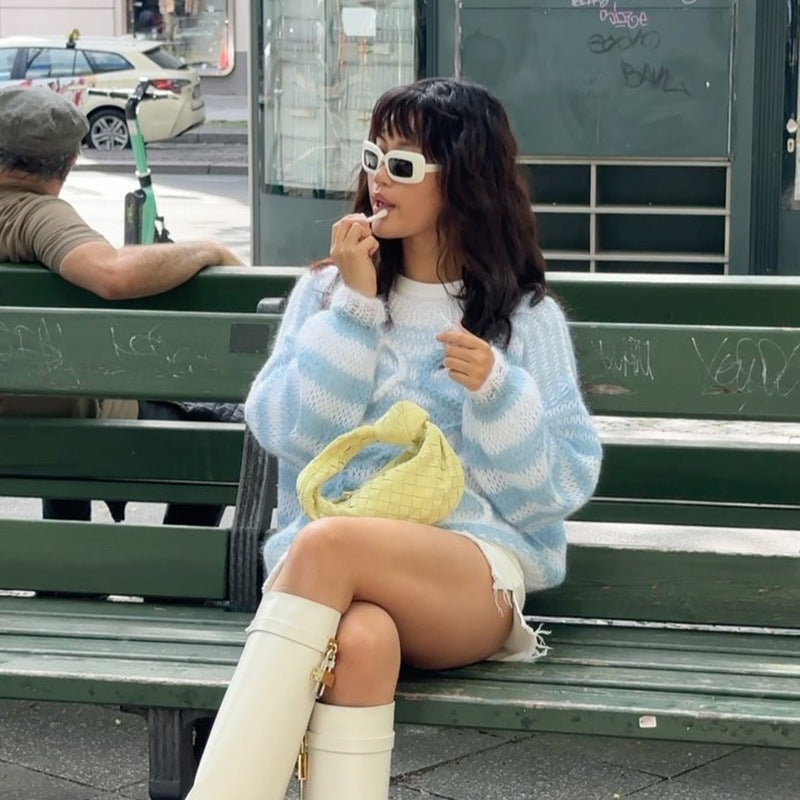 Model wearing a cozy blue and white striped sweater, sitting on a park bench with a yellow handbag and white knee-high boots.