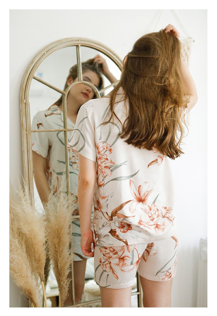 Floral print silk loungewear set featuring a relaxed button-up shirt and matching shorts, styled elegantly against a mirror backdrop.