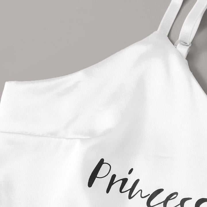 Close-up of a white satin lingerie top featuring the word "Princess" in elegant black script on the front, highlighting adjustable straps and a soft fabric texture.