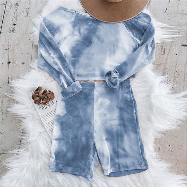 Blue tie-dye loungewear set featuring a cropped long-sleeve top and matching shorts, laid out on a fluffy surface.