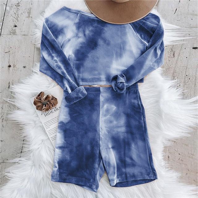 Blue tie-dye loungewear set featuring a cropped long sleeve top and matching shorts, styled with a brown wide-brim hat and hair scrunchie.