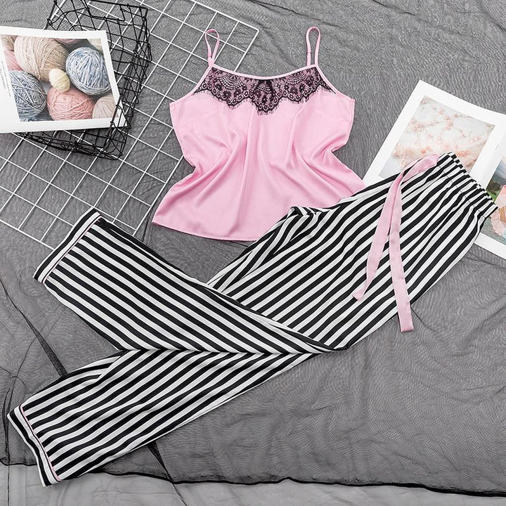 Pink satin camisole with black lace trim paired with black and white striped pajama pants on a textured gray background.