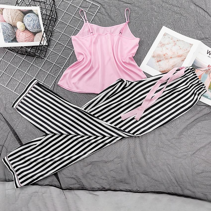 Pink satin camisole top paired with black and white striped lounge pants, styled on a textured gray background.