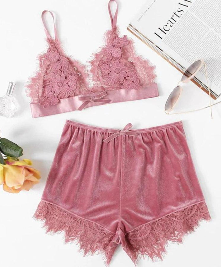 Lace bralette and matching shorts set in soft pink with floral detailing and satin finish, styled with accessories and a magazine.